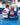 Kids in white and blue Gracie Barra kimonos with gray belts sitting on a blue mat during class, red Barra Shield patches on their backs
