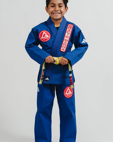 Child wearing a blue Pro Lite Comp Youth Kimono by adidas with Gracie Barra logos on a plain background