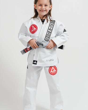 Child wearing a white Pro Lite Comp Youth Kimono by adidas with Gracie Barra branding, standing against a white background
