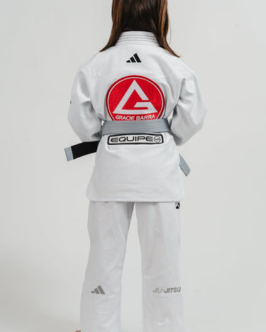 Child wearing the back of a white Pro Lite Comp Youth Kimono by adidas featuring Gracie Barra and Equipe branding on a plain background