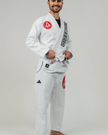 Side angle view of man wearing Pro Lite Comp Men’s Kimono by adidas in white with Gracie Barra and adidas branding, barefoot on light gray background