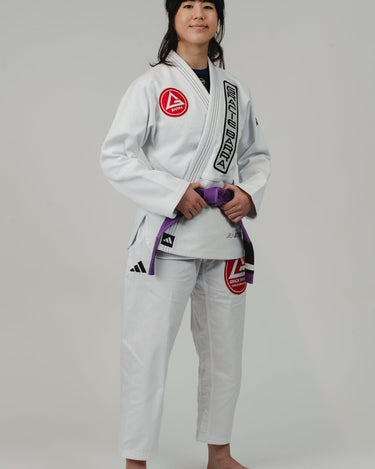 Woman in the white adidas Pro Lite Comp Kimono with Gracie Barra patches, posed at a right-facing angle against a white background.