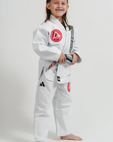 Child wearing the right side of a white Pro Lite Comp Youth Kimono by adidas with visible Gracie Barra branding on a plain background