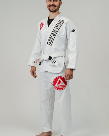 Side angle view from left of man wearing Pro Lite Comp Men’s Kimono by adidas in white with Gracie Barra and adidas branding, barefoot on light gray background