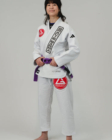 Woman in the white adidas Pro Lite Comp Kimono with Gracie Barra patches, posed at a left-facing angle against a white background.