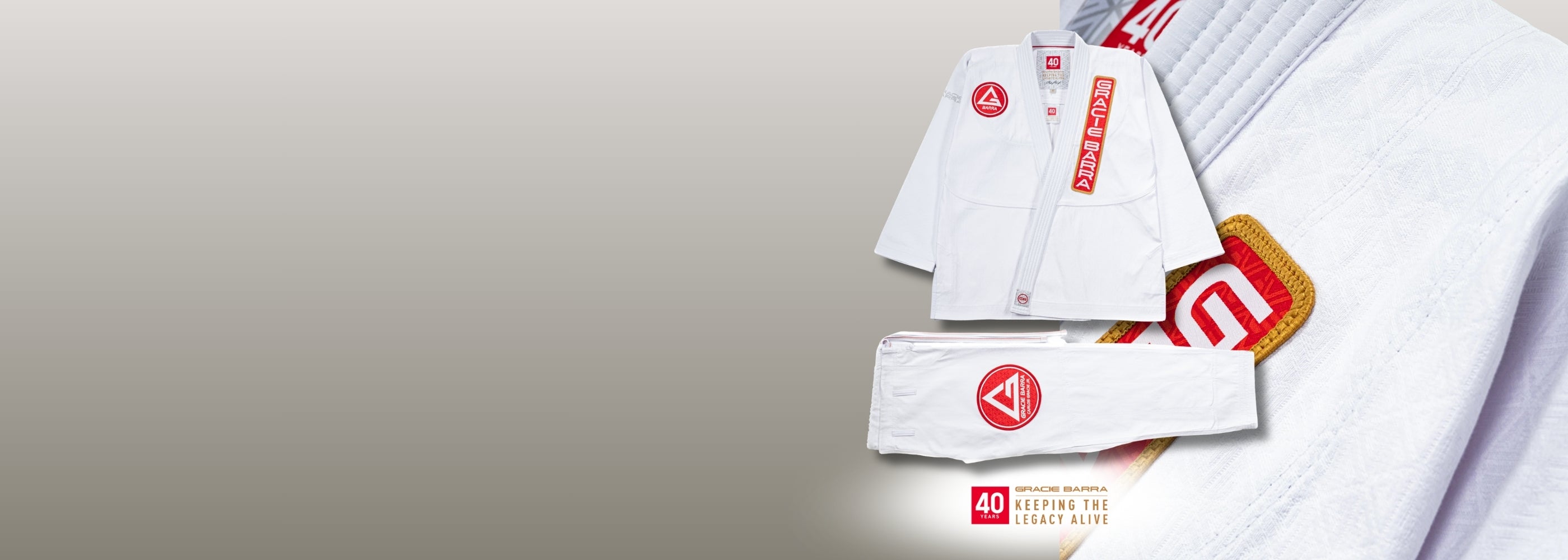 Gracie Barra 40 Years — Keeping the Legacy Alive. White kimono jacket and pants with red Barra Shield patch, displayed alongside a red-and-gold anniversary patch on a neutral gradient background.