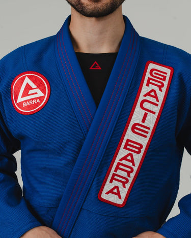 Close-up of front collar on men’s blue Pro Lite Comp Kimono by adidas with red Gracie Barra patch on light gray background