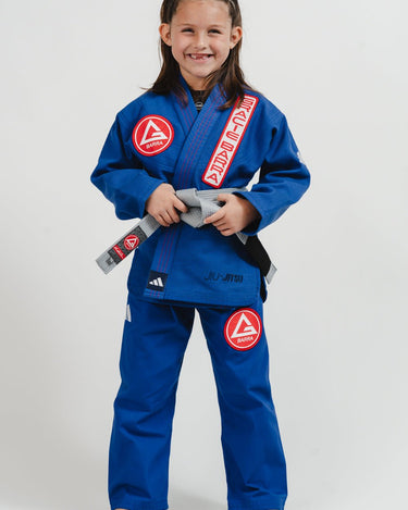 Child wearing a blue Pro Lite Comp Youth Kimono by adidas with Gracie Barra patches, standing against a plain background