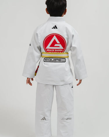 Child wearing a white Pro Lite Comp Youth Kimono by adidas with Gracie Barra and Equipe branding on the back, against a white background