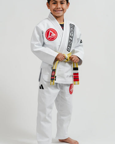 Child wearing a white Pro Lite Comp Youth Kimono by adidas with Gracie Barra branding, photographed from the right on a plain background