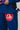 Close-up of a woman wearing a blue Pro Lite Comp Kimono by adidas, featuring black "JIU-JITSU" embroidery and a red Gracie Barra patch on the left pant leg, against a light background.