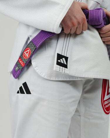 Detail of white Pro Lite Comp Kimono by adidas, highlighting the hip area with adidas and Gracie Barra logos visible on the pants and jacket against a plain background.