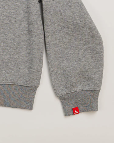 Sleeve detail of grey Arte Suave V2 kids crewneck sweatshirt by Gracie Barra, featuring red woven tag with Legacy G logo near ribbed cuff.