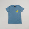 Full view of the Arte Suave V2 kids’ T-shirt in blue by Gracie Barra, featuring a small yellow Legacy G logo above “Brazilian Jiu-Jitsu” text on the left chest, and a red sleeve tag, displayed on a light gray background.