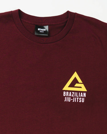 Close-up of Arte Suave V2 men’s maroon T-shirt featuring yellow Legacy G logo and “BRAZILIAN JIU-JITSU” text in white on the left chest, displayed on a white background.