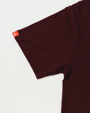 Close-up of Arte Suave V2 men’s maroon T-shirt sleeve with red woven tag featuring white Legacy G logo, displayed on a white background.