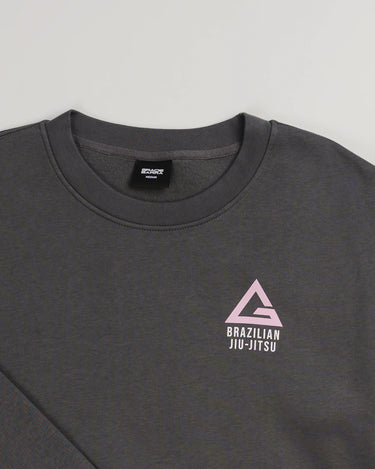 Close-up of dark grey Arte Suave V2 women’s crewneck sweatshirt by Gracie Barra, featuring pink Legacy G chest logo with “Brazilian Jiu-Jitsu” text in white.
