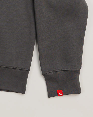 Sleeve detail of dark grey Arte Suave V2 women’s crewneck sweatshirt by Gracie Barra, featuring red woven tag with Legacy G logo near ribbed cuff.