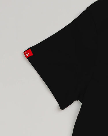 Close-up of the Arte Suave V2 women’s black T-shirt sleeve featuring a small red woven Legacy G logo tag, displayed on a light gray background.