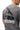 Arte Suave V3 Mens Tee in gray, back view on the model. Full-back print: white 'Arte Suave' script, black tonal figure, white 'Gracie Barra' wordmark.