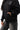 Arte Suave V3 Womens Hoodie in black, torso close-up with hand in the kangaroo pocket: silver Legacy G logo, white 'Arte Suave' script, ribbed cuff.