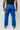 Athlete modeling blue Atleta competition gi pants from behind, showing the red Gracie Barra print on the back waist and straight-leg competition cut