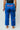 Athlete modeling blue Atleta women's competition gi pants from behind, showing the red Gracie Barra print on the back waist and relaxed straight-leg fit