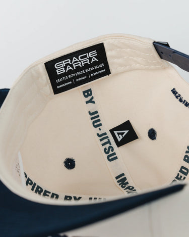 Inside view of Barra Cap in natural showing woven “Gracie Barra” label, interior taping with “Inspired by Jiu-Jitsu” text, and small black Legacy G tag.