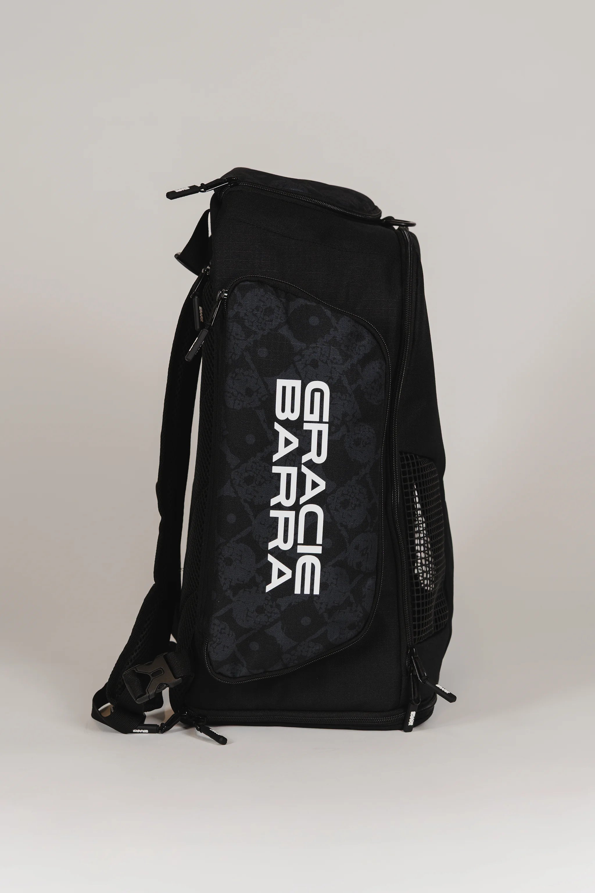 Side view of Black Barra da Tijuca Backpack showing the “Gracie Barra” wordmark over the patterned calçadão fish print panel, with mesh ventilation pocket and ripstop fabric.