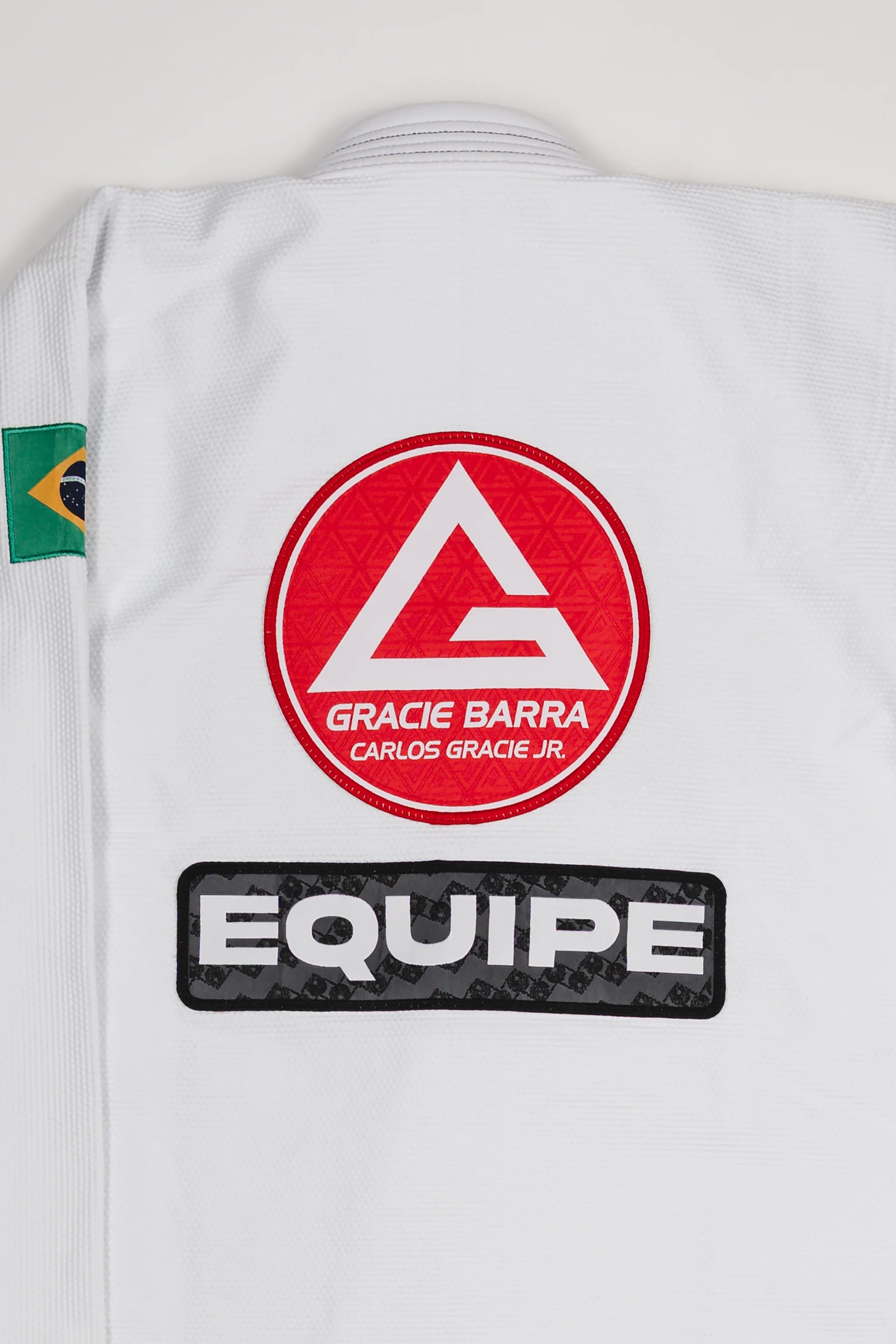 Back view of the Barra da Tijuca White Kimono jacket showing the large Red Shield logo and the EQUIPE patch, with the Brazilian flag patch on the shoulder.