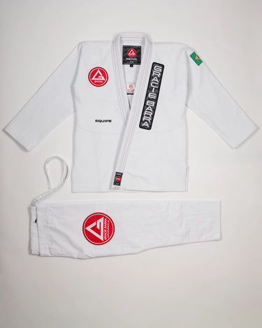 Full front view of the Barra da Tijuca White Kimono, showing the jacket with Red Shield patch, Gracie Barra lapel patch, EQUIPE embroidery, Brazilian flag shoulder patch, and matching pants with the Red Shield patch laid below.