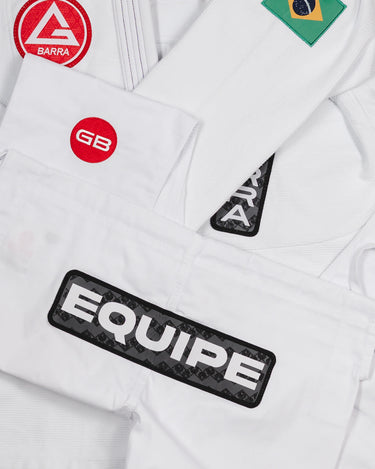 Folded Barra da Tijuca White Kimono pants laid over the jacket to display all key patches, including the Red Shield, GB circle patch, EQUIPE patch, Gracie Barra lapel patch, and Brazilian flag shoulder patch.