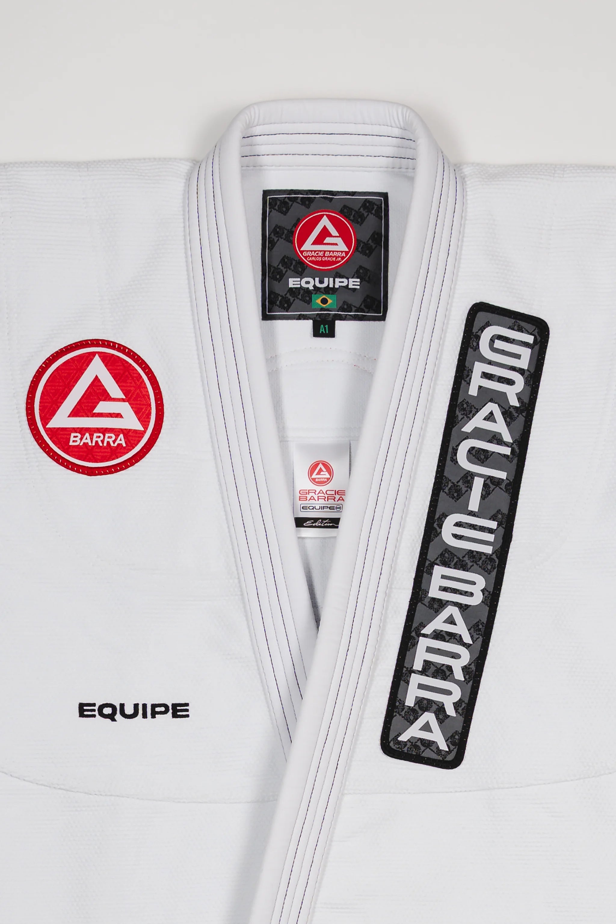 Front view of the Barra da Tijuca Kimono showing the Red Shield patch, Gracie Barra lapel patch, and EQUIPE embroidery on a white jacket.