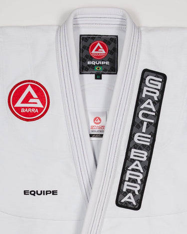 Front view of the Barra da Tijuca Kimono showing the Red Shield patch, Gracie Barra lapel patch, and EQUIPE embroidery on a white jacket.