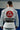 Back view of a Gracie Barra professor wearing the Barra da Tijuca White Kimono, showcasing the large red Gracie Barra back patch and EQUIPE patch while standing on the academy mats.