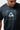 Close-up of the chest graphic on the black Terra Mar tee: white Legacy G triangle and BARRA DA TIJUCA wordmark in a gray boardwalk-tile square.