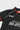 Angled front view of the black Barra Origins kids jersey showing the red trimmed collar, white piping, and stacked Gracie Barra wordmark.