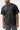 Front three-quarter view of the washed black Gracie Barra Emblem Tee showing the ribbed crew neck, tonal Stacked logo embroidery and red sleeve tag.