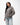 Emblem Womens Hoodie in Gray — three-quarter front on model with hand in the pouch pocket, showing the tonal Gracie Barra chest emblem over light-wash jeans.