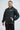 Three-quarter view of the black Equipe windbreaker worn with a hand in the side pocket, showing the red GRACIE BARRA sleeve print.