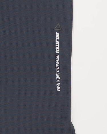 Close-up of grey Equipe Motion Men’s Tee side seam with reflective ‘Jiu-Jitsu Organized Like a Team’ print and Legacy G icon on breathable fabric.
