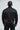 Back view of the black Equipe Warm Up Jacket showing the white Jiu-Jitsu print and Brazil flag patch above the elasticated hem.
