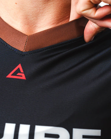 GB Essentials Women’s Rashguard in brown colorway, close-up of collar with reinforced stitching, red GB Legacy G logo, and stretch fabric detail.