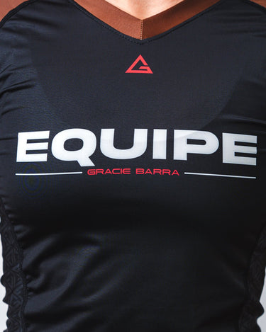 GB Essentials Women’s Rashguard in brown colorway, close-up of chest with bold EQUIPE wordmark, red GB Legacy G logo at collar, and contoured side panels.