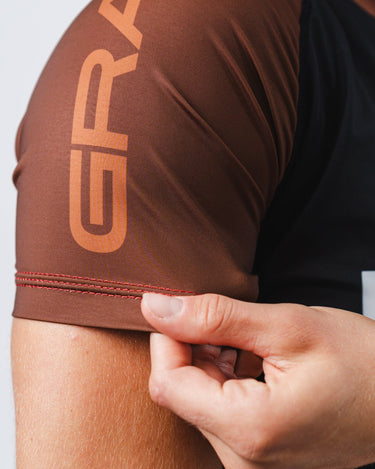 GB Essentials Women’s Brown Belt Ranked Rashguard close-up of sleeve with flatlock stitching and split stacked logo on the shoulder.