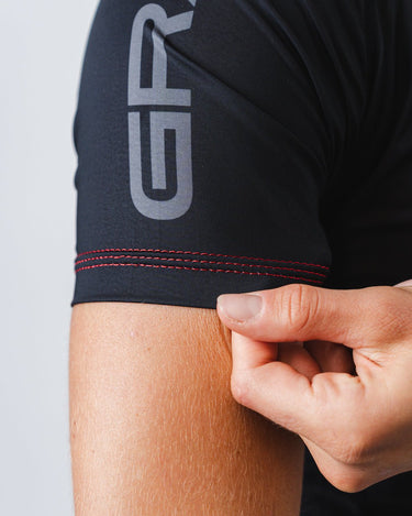 GB Essentials Womens Ranked Rashguard in black with split Stacked Logo sleeve detail, red contrast stitching, and stretch fabric construction