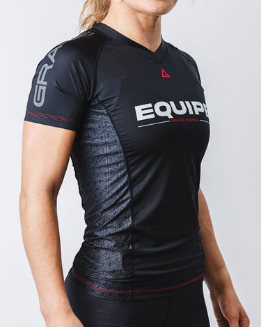 GB Essentials Women’s Ranked Rashguard in black, front-side view showing EQUIPE wordmark, split stacked logo on the sleeve, and geometric side panels.