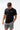 Flow Men's Tech Tee in black, full-length front view on a male model looking down, with the white Gracie Barra Stacked logo on the left chest
