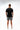 Flow Men's Tech Tee in black, full-length back view on a male model showing the small white Brazilian Jiu-Jitsu graphic on the upper back