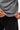 Flow Men's Tech Tee in dark grey, close-up of a model holding the curved hem out with both hands to show the fabric stretch